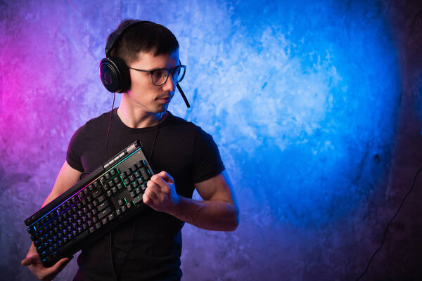 Professional Boy Gamer holding gaming keyboard over colorful pink and blue neon lit wall. Gaming gamers concept