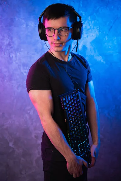 Professionelle Boy-Gamer halten Gaming-Tastatur über bunte rosa und blaue neonbeleuchtete Wand. Spielemacher-Konzept — Stockfoto