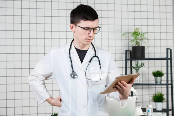 Tablet bilgisayar kullanarak dalgın yakışıklı genç erkek doktor. Tıp kavramı teknolojileri