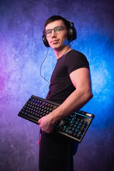 Computer nerd with keyboard over colorful pink and blue neon lit wall