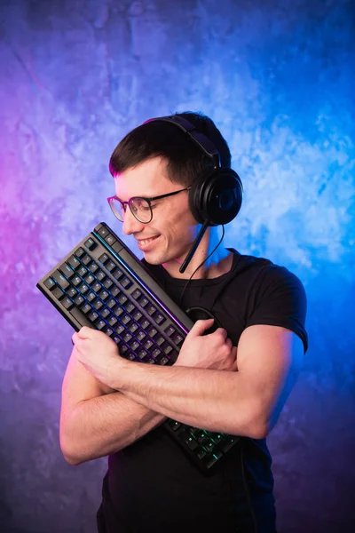 Professional Boy Gamer holding gaming keyboard over colorful pink and blue neon lit wall. Gaming gamers concept — Stock Photo, Image