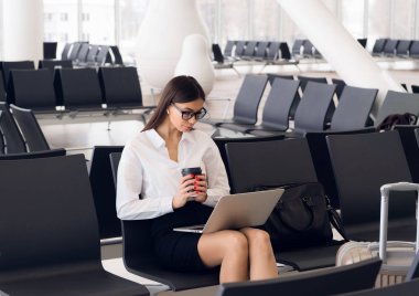 Laptop Havaalanı salonunda çalışan casual kadın. Onun uçuş Havaalanı terminalinde bekliyor, sandalyede oturan ve dizüstü bilgisayarda yazarak kadın
