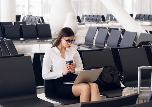 Laptop Havaalanı salonunda çalışan casual kadın. Onun uçuş Havaalanı terminalinde bekliyor, sandalyede oturan ve dizüstü bilgisayarda yazarak kadın