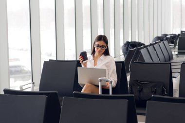 Laptop Havaalanı salonunda çalışan casual kadın. Onun uçuş Havaalanı terminalinde bekliyor, sandalyede oturan ve dizüstü bilgisayarda yazarak kadın
