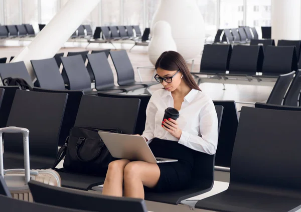Laptop Havaalanı salonunda çalışan casual kadın. Onun uçuş Havaalanı terminalinde bekliyor, sandalyede oturan ve dizüstü bilgisayarda yazarak kadın