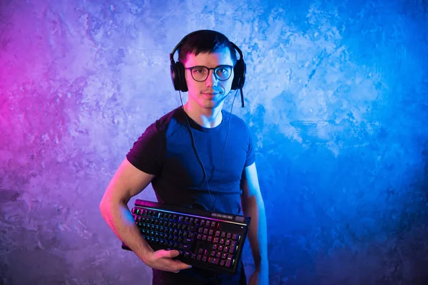 Professional Boy Gamer holding gaming keyboard over colorful pink and blue neon lit wall. Gaming gamers concept