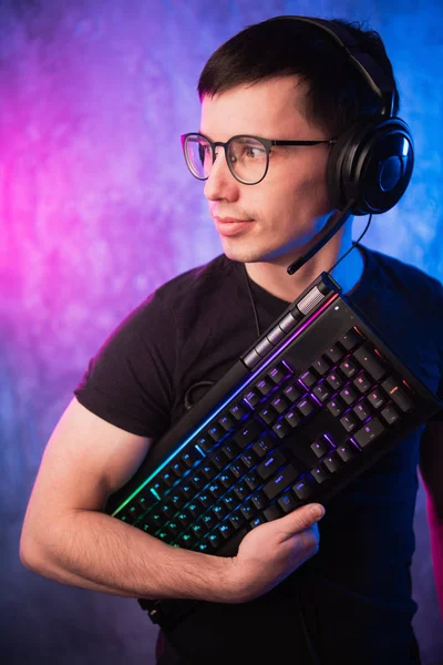 Computer-Nerd mit Tastatur über bunte rosa und blaue neonbeleuchtete Wand — Stockfoto