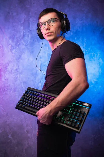 Computer nerd with keyboard over colorful pink and blue neon lit wall