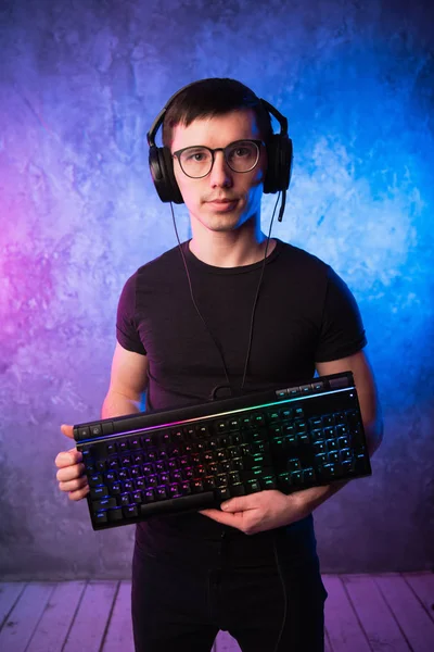 Professionelle Boy-Gamer halten Gaming-Tastatur über bunte rosa und blaue neonbeleuchtete Wand. Spielemacher-Konzept — Stockfoto