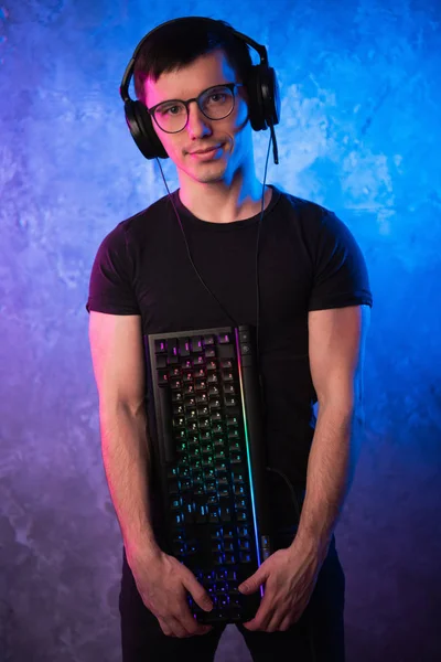Professionelle Boy-Gamer halten Gaming-Tastatur über bunte rosa und blaue neonbeleuchtete Wand. Spielemacher-Konzept — Stockfoto