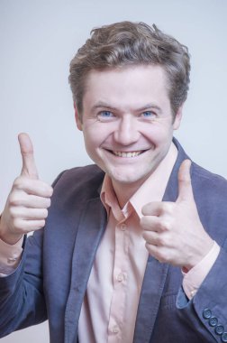 Beyaz arka plan üzerinde başparmak gösterilmesini genç zarif beyaz elbise mutlu gülümseyen mavi gözlü bir adam portresi.