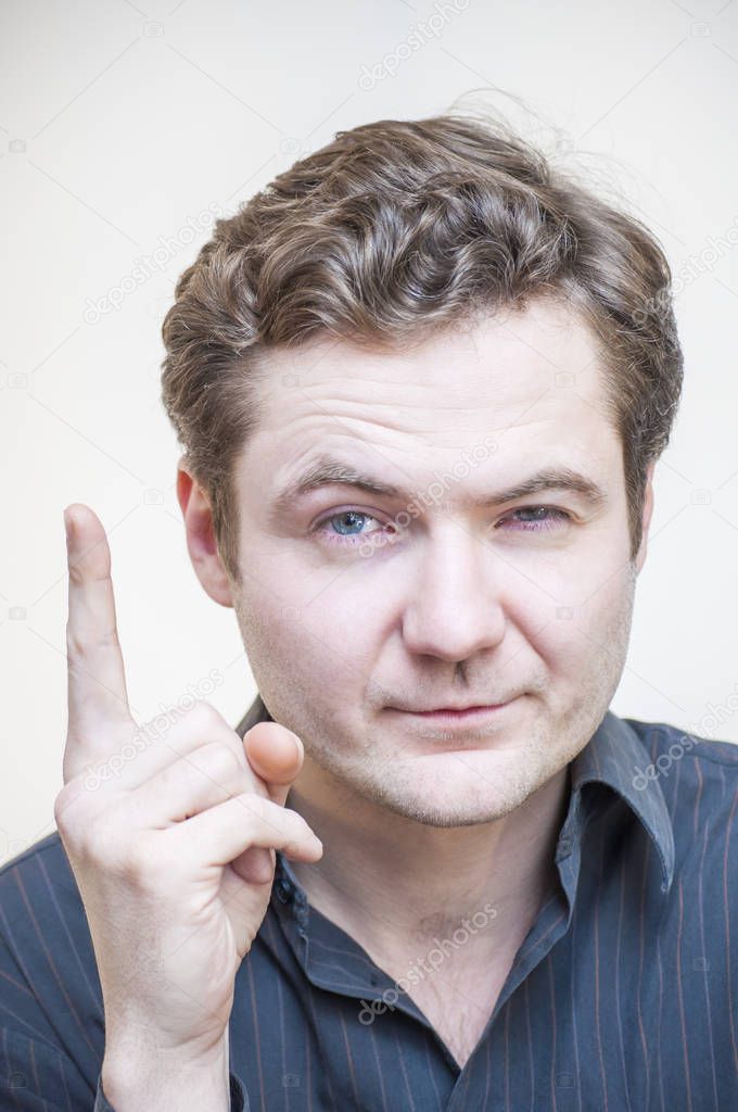 Portrait of young cunning tricky blue-eyed man got great idea and pointing with finger up on white background.