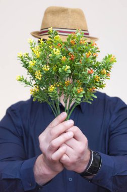 Yapay sarı ve turuncu çiçekler yüzünü önünde tutan genç atletik zarif adam portresi.