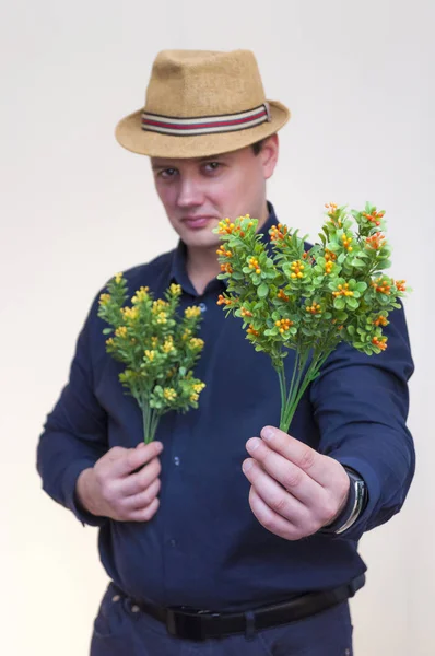 年轻优雅的男子纵向蓝色衬衫和夏天帽子持有人工黄色和橙色的花朵在双手 — 图库照片