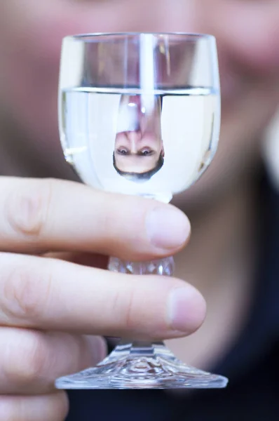 Portrait of young Caucasian Ethnicity man with blue shirt and his upside down reflection in Vodka glass shot.