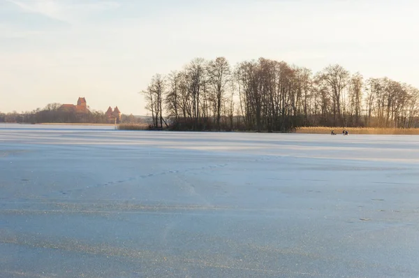 Still winter time, frozen lakes, lonely fishermen sitting on the ice, low sun, long shadows, lonely piers with empty bollards. Lake Galve is a lake in Trakai Lithuania. It has 21 islands.