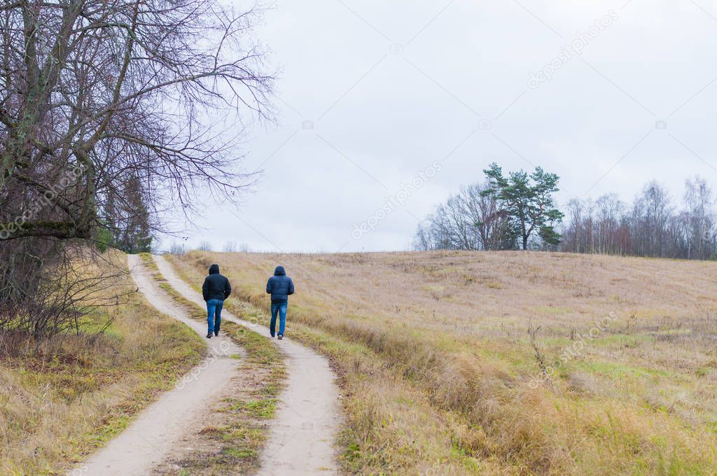 Two men walking by the rural road at fall. Overcast weather almost every day. But the fresh air is tasty and it is a pure pleasure to take a little walk through the country surroundings.