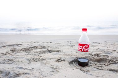 Kochi, Kerala, Hindistan - 11 Ocak 2015: Plastik Coca Cola şişesi sol tarafta Kochi Umman Denizi plajda kuma ayak izi neredeyse boş.