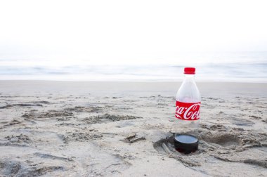 Kochi, Kerala, Hindistan - 11 Ocak 2015: Plastik Coca Cola şişesi sol tarafta Kochi Umman Denizi plajda kuma ayak izi neredeyse boş.