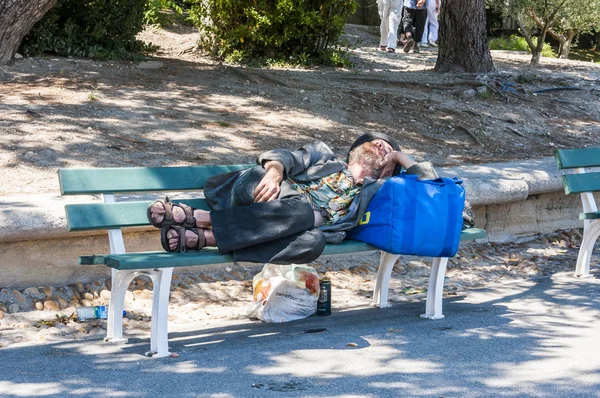 Avignon, Fransa - 24 Temmuz 2011: Evsiz adam Avignon Festivali kapalı sırasında tezgah altında bıçakla Eski kentte oudoors uyuyor. Ona yakın insanlar istirahat, oturan, tarafından yürüyüş.