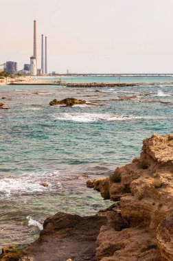 Caesarea, İsrail - 22 Mayıs 2012: Kayalar sahilde kayalık Akdeniz sahil suları ve Orot Rabin, bir kömür yakıtlı elektrik santrali