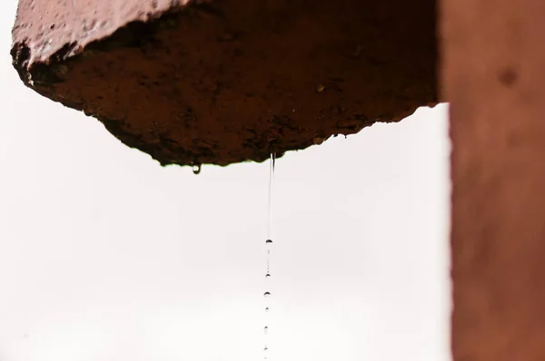 Raindrops falling down in a rows from concrete construction frame during the rain