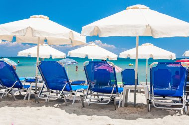 Paralia, Yunanistan - 15 Haziran 2013: mavi şezlonglar, beyaz güneş şemsiye şemsiye arka planda Yunan Paralia resort şehir sıcak Ege Denizi ile kumsallarında turistlerin dinlenme,