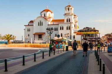 Paralia, Yunanistan - 15 Haziran 2013: Aziz Fotini Kilisesi veya aziz Paraskevi Kilisesi Paralia resort, Yunanistan plajında yer. Sokak, Ege Denizi sahil yürüyüş insanlar Turizm
