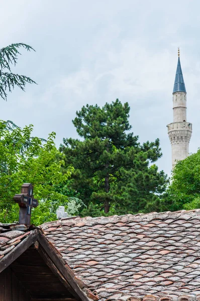 Skopje, Macedonia - June 10, 2013: Catholic wooden cross on top of the roof on foreground and Mustafa Pasha Mosque tower on the background in Skopje, Macedonia