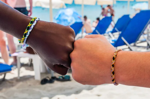 两个不同种族的人的两个拳头 每个手腕上的彩色线上都有编织的手镯 在友谊与和平标志的象征意义上互相触摸 — 图库照片