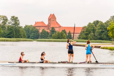 Trakai, Litvanya - 26 Temmuz 2013: Dört sporcu kızlar coxed dört kürek teknede Galve göl üzerinde Trakai Kalesi ile arka plan. Coxed dört rekabet kürek Sporda kullanılan bir kürekli sandal geldi