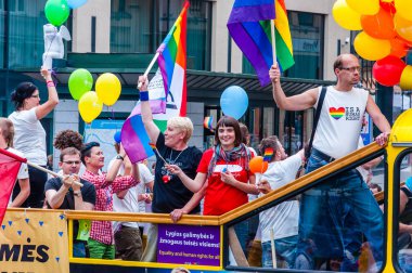 Vilnius, Litvanya - 27 Temmuz 2013: Pride parade olay eylem. Gökkuşağı bayrağı sarı açık üst veri yolunda onun yükseltilmiş kol ayakta ile gururlu adam göstericiler tam renkli balonlarla süslenmiş