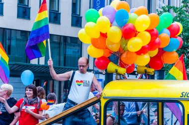 Vilnius, Litvanya - 27 Temmuz 2013: Pride parade olay eylem. Gökkuşağı bayrağı sarı açık üst veri yolunda onun yükseltilmiş kol ayakta ile gururlu adam göstericiler tam renkli balonlarla süslenmiş
