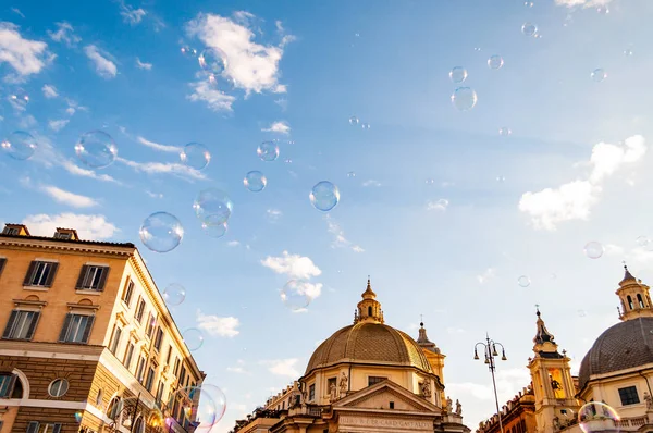 Rome, Italy - November 18, 2018: Soap bubbles flying on Piazza del Popolo, People Square in Rome surrounded by ancient churches like Santa Maria in Montesanto with its great domes and bell towers