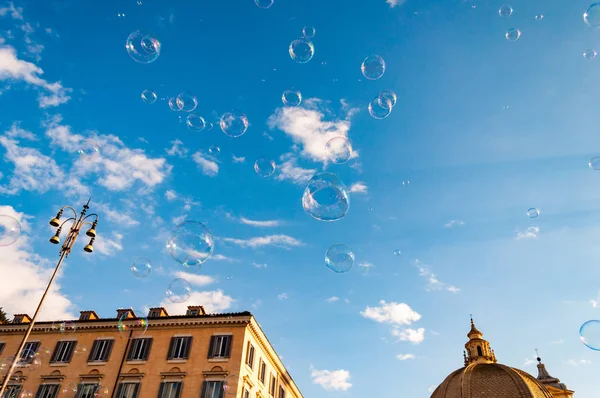 Rome, Italy - November 18, 2018: Soap bubbles flying on Piazza del Popolo, People Square in Rome surrounded by ancient churches like Santa Maria in Montesanto with its great domes and bell towers