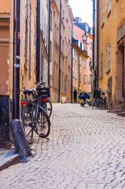 Rahat Ortaçağ kaldırım taşı yürüyen insanlar, sarı turuncu kırmızı binalar cephe Gamla Stan, Stockholm eski şehir içinde park edilmiş bisiklet, çalışan işletmeler ile sokak