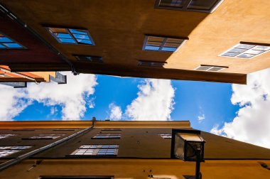 Aşağıdan bir rahat dar Ortaçağ sokak sarı turuncu kırmızı binaları cephe Gamla Stan'da, eski Stokholm şehir, İsveç arka plan üzerinde parlak mavi gökyüzü ile çatılarda görüntülemek