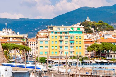 Sanremo limanından deniz tekneleri, gemiler ve yatlarla dolu eski şehir kıyısı manzarası ve arka planda Liguria manzarası.