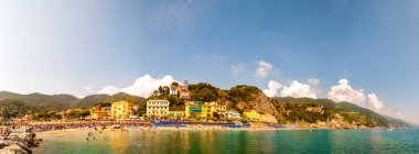 Kayalık marina manzarası, Ligurian Denizi 'nin berrak suyu, deniz gemileri, insanlarla dolu plaj, Monterosso Al Mare, Cinque Terre, İtalya' daki liman binaları.