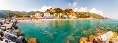 Kayalık marina manzarası, Ligurian Denizi 'nin berrak suyu, deniz gemileri, insanlarla dolu plaj, Monterosso Al Mare, Cinque Terre, İtalya' daki liman binaları.