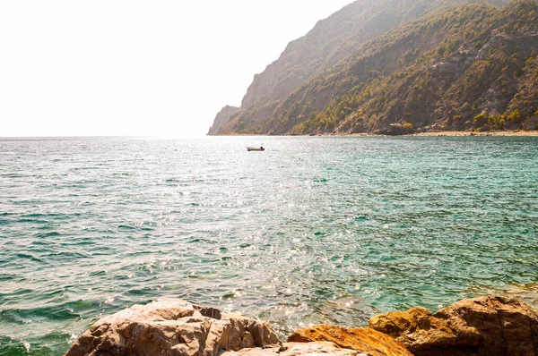 Rocas del puerto deportivo en primer plano y un solo barco cerca de la costa rocosa con altas montañas verdes y rayos de sol penetrantes por detrás en el fondo en Monterosso Al Mare, Cinque Terre — Foto de Stock