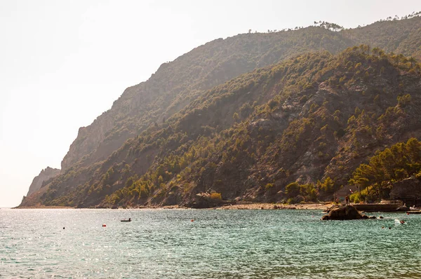 Playa rocosa cerca de la costa alta, montañas verdes y rayos de sol penetrantes por detrás en el fondo en Monterosso Al Mare, Cinque Terre, Italia — Foto de Stock