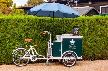 Londra, Birleşik Krallık - 15 Eylül 2017: Kraliyet Parklarının klasik dondurma bisikleti ve yeşil doğal çitin yanında duran mavi şemsiye