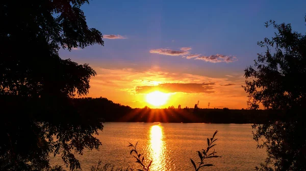 Amazing sunrise over a lake. Rays of the sun reflecting on the water. Holiday landscape by the sea. Quiet relaxing scene with a beautiful colorful sky. Silhouette of vegetation in the foreground.