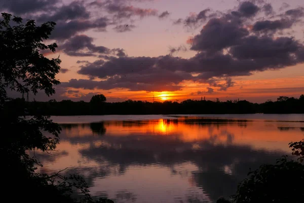 Amazing sunrise in rural scene. Symmetry of the sky in a lake at sunset. Clouds reflecting on the water. Quiet relaxing scene with a beautiful colorful cumulonimbus.