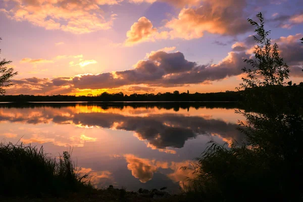 Amazing sunrise in rural scene. Symmetry of the sky in a lake at sunset. Clouds reflecting on the water. Quiet relaxing scene with a beautiful colorful cumulonimbus.