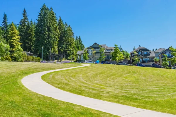 Paved pathway over green lawn on the slope in front of new townhouses