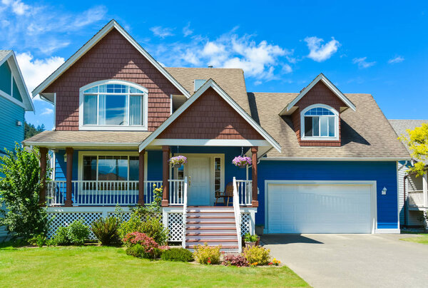 Blue residential house with concrete driveway in front and blue sky background.