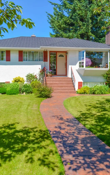 Average family house with green lawn and trees in front on blue sky background