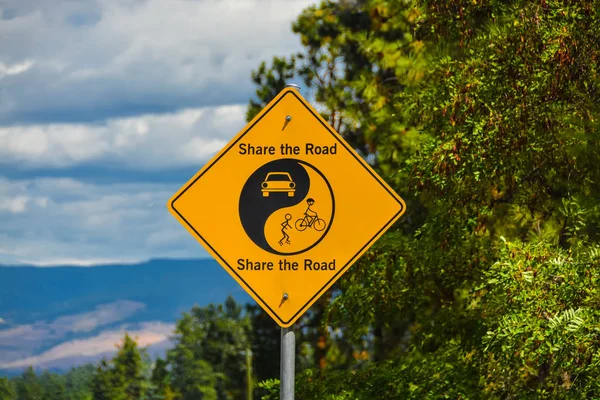 Compartilhe o sinal amarelo Estrada em folhas verdes e fundo céu azul . — Fotografia de Stock